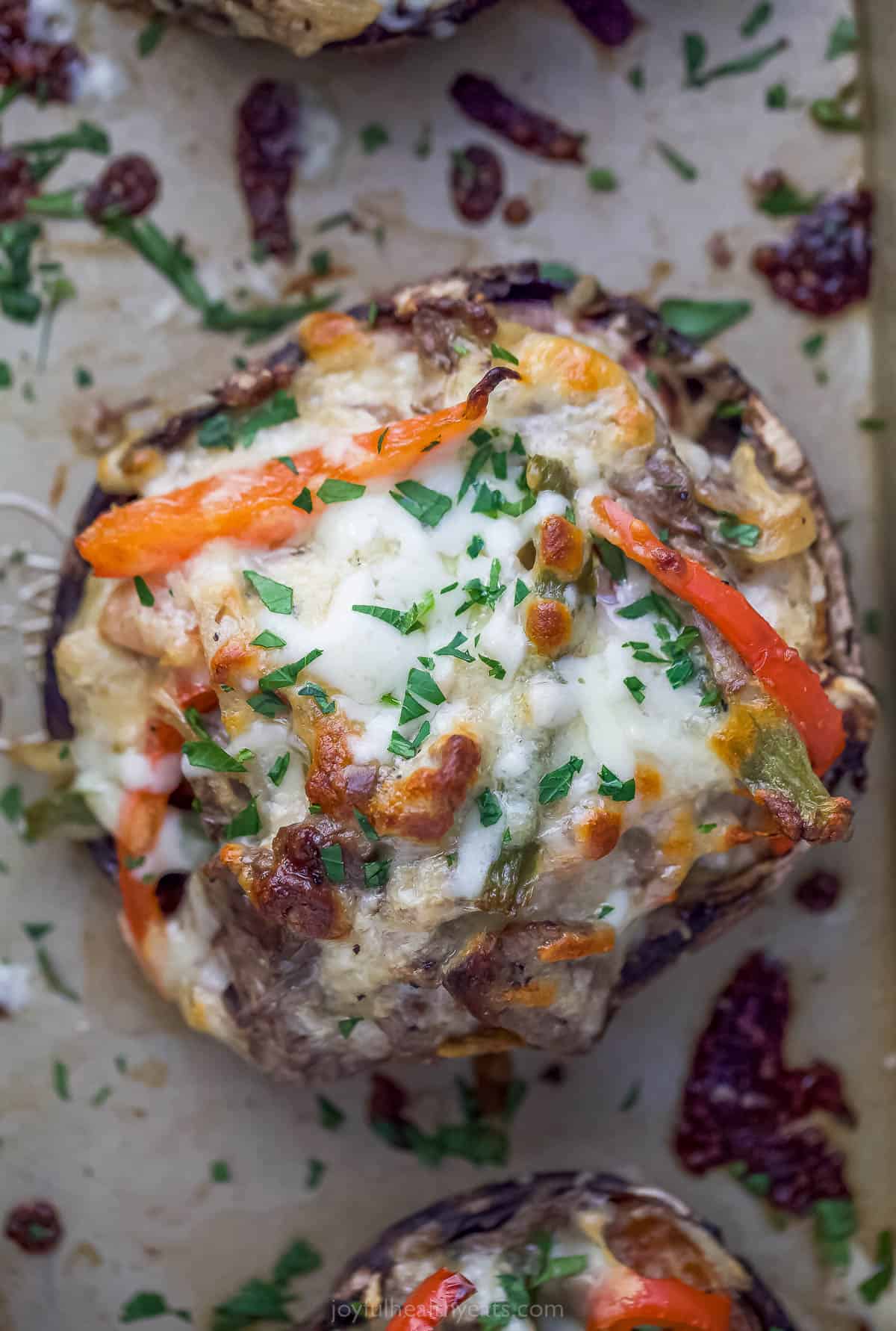 These Easy 30-Minute Philly Cheese Steak Stuffed Mushrooms are packed with tender steak, sautéed vegetables, and gooey cheese. stuffed mushroom on a sheet tray with peppers, melted cheese, and herbs