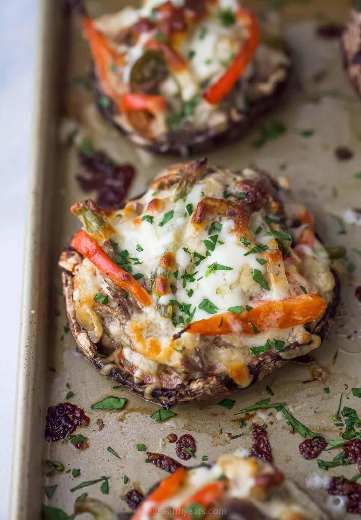 stuffed mushroom on a sheet tray with peppers, melted cheese, and herbs