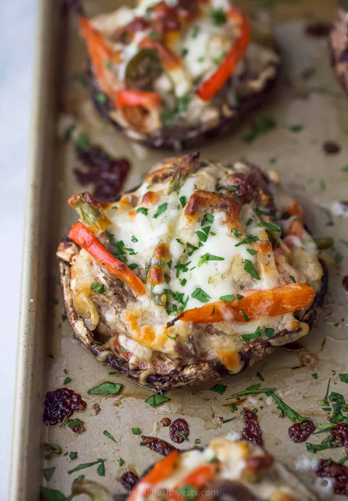 These Easy 30-Minute Philly Cheese Steak Stuffed Mushrooms are packed with tender steak, sautéed vegetables, and gooey cheese. stuffed mushroom on a sheet tray with peppers, melted cheese, and herbs