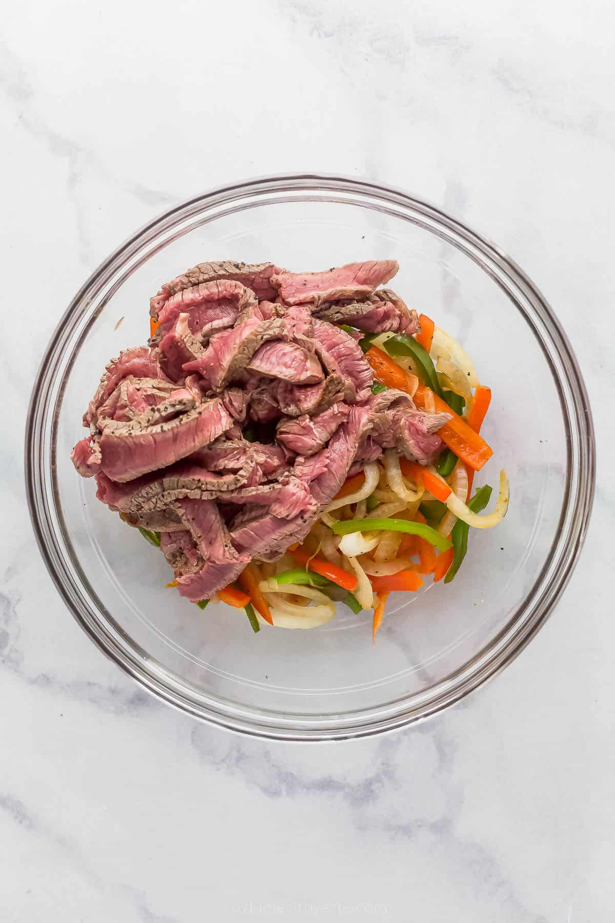 sliced steak and vegetables in a gl، bowl