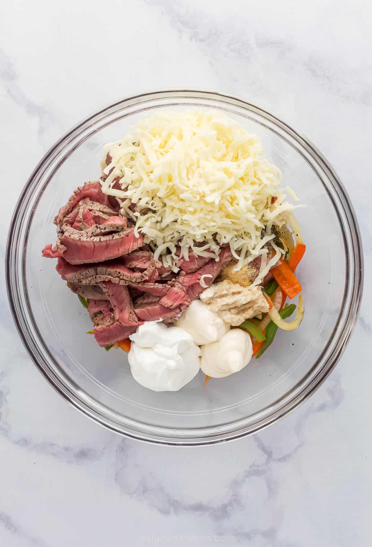 These Easy 30-Minute Philly Cheese Steak Stuffed Mushrooms are packed with tender steak, sautéed vegetables, and gooey cheese. cheese, slice vegetables, and dollops of cream sauce in a glass bowl