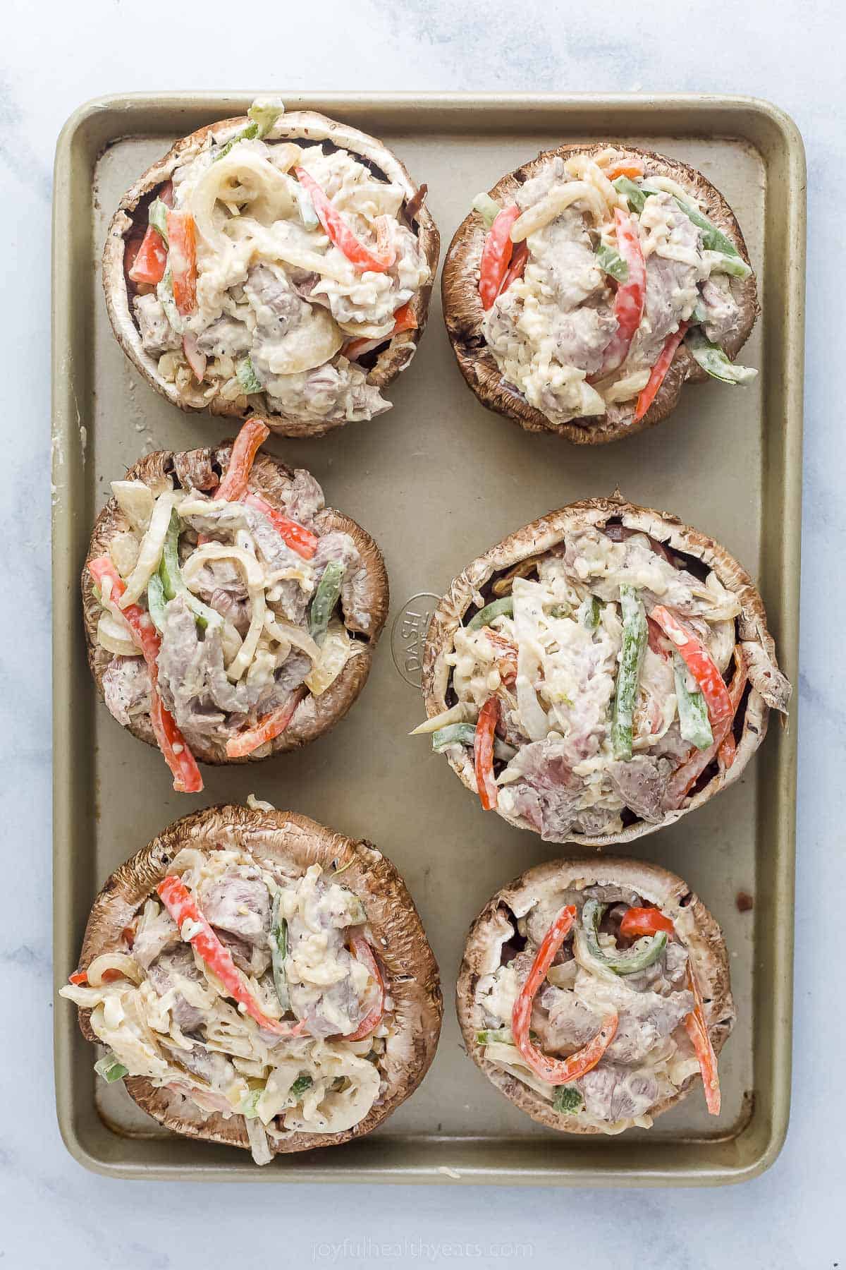 about to be cooked philly cheesesteak stuffed mushrooms on a sheet tray garnished with fresh herbs