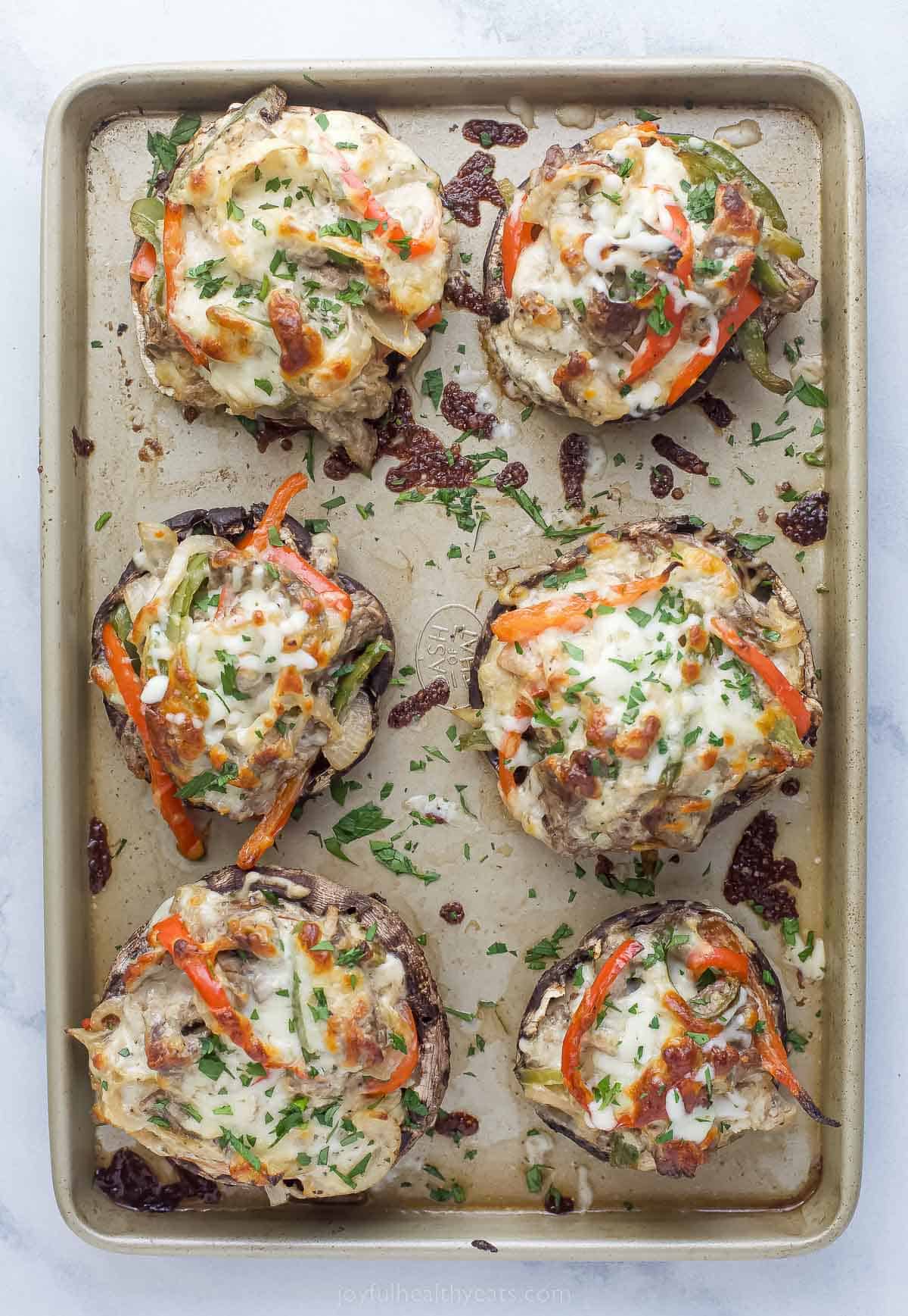 These Easy 30-Minute Philly Cheese Steak Stuffed Mushrooms are packed with tender steak, sautéed vegetables, and gooey cheese. philly cheesesteak stuffed mushrooms on a sheet tray garnished with fresh herbs