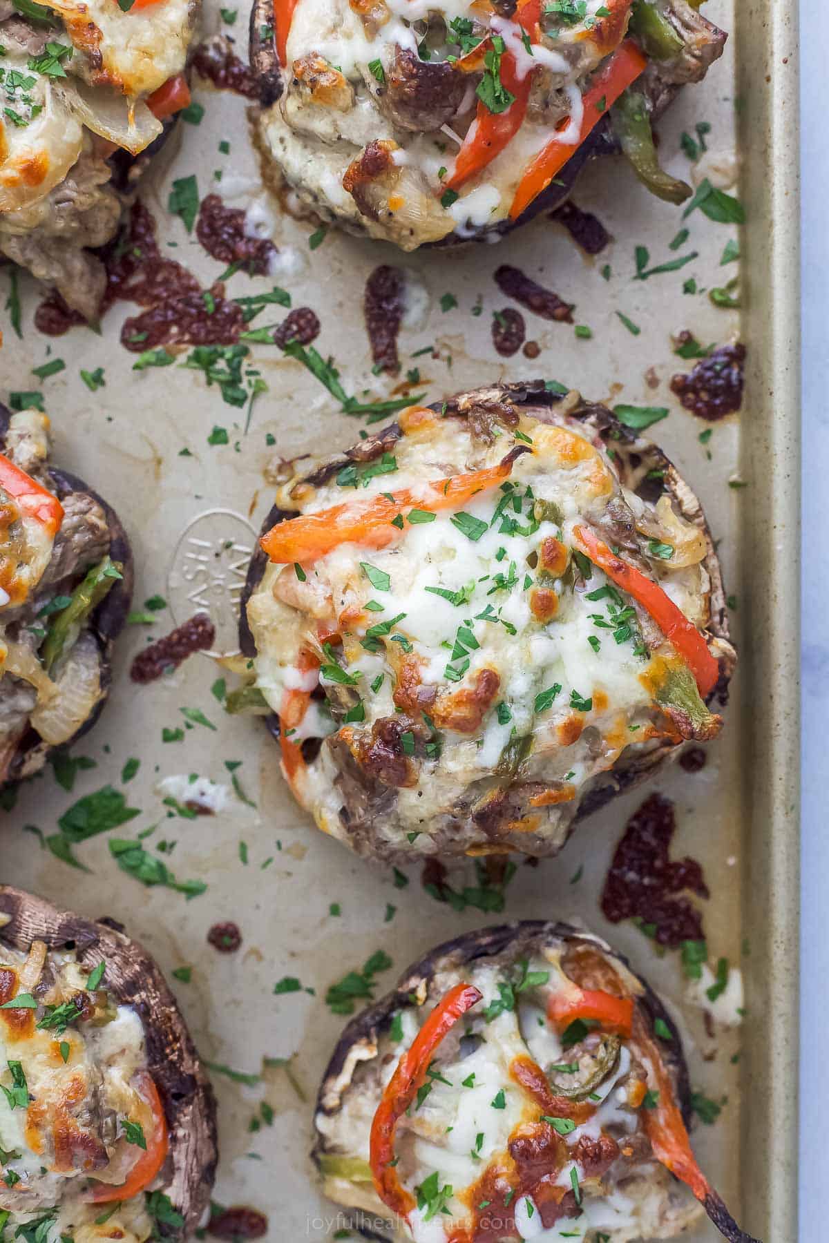 These Easy 30-Minute Philly Cheese Steak Stuffed Mushrooms are packed with tender steak, sautéed vegetables, and gooey cheese. philly cheesesteak stuffed mushrooms on a sheet tray garnished with fresh herbs