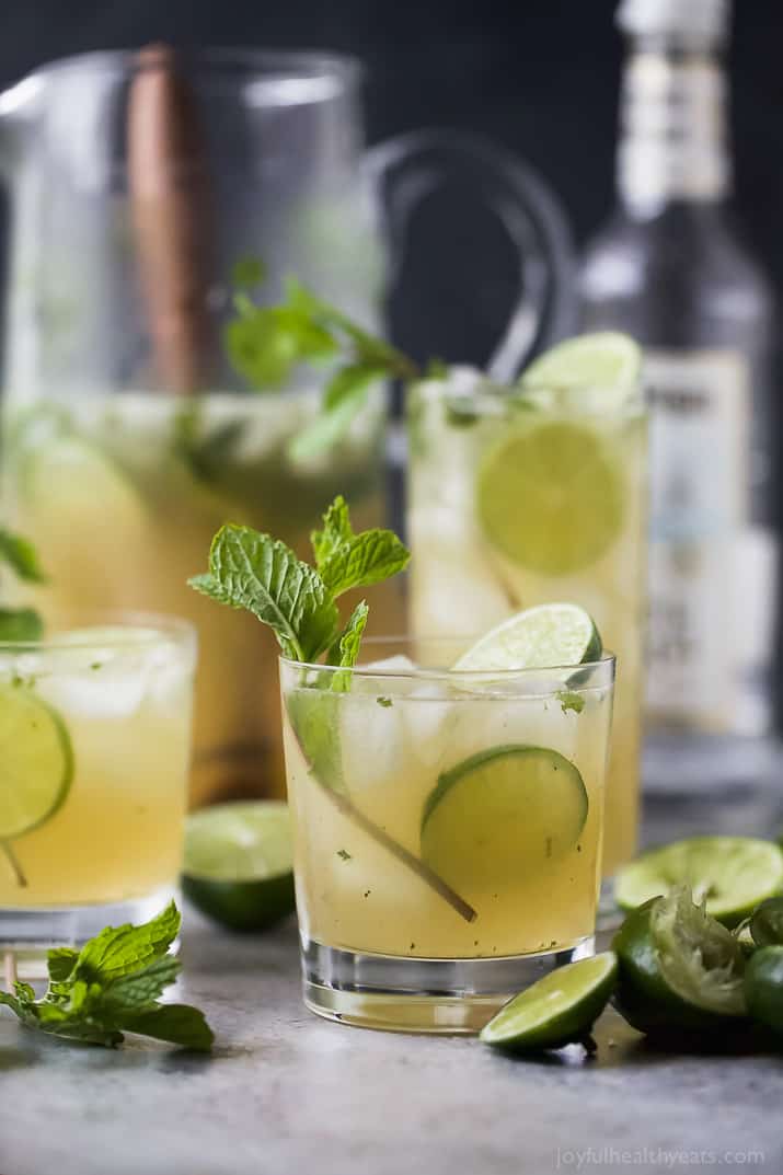 Mojito in a pitcher and several glasses with mint and lime garnish