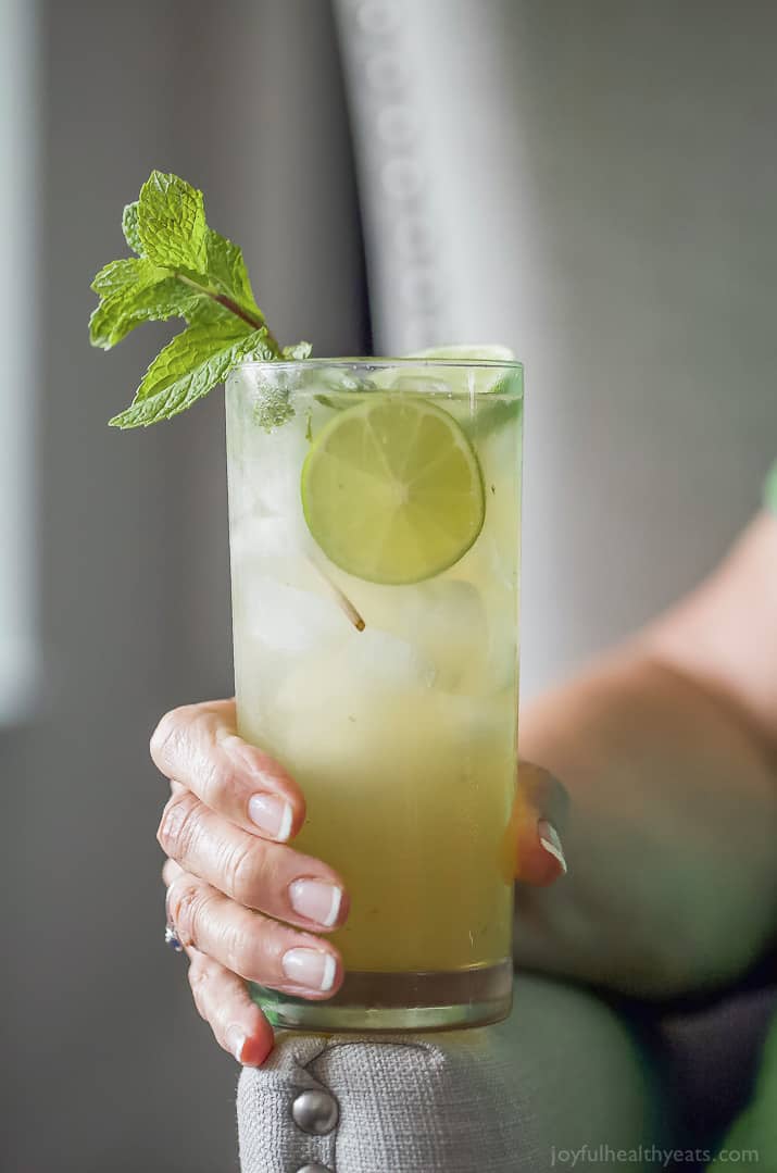 A hand holding a tall glass of Mojito Recipe with mint and lime garnish