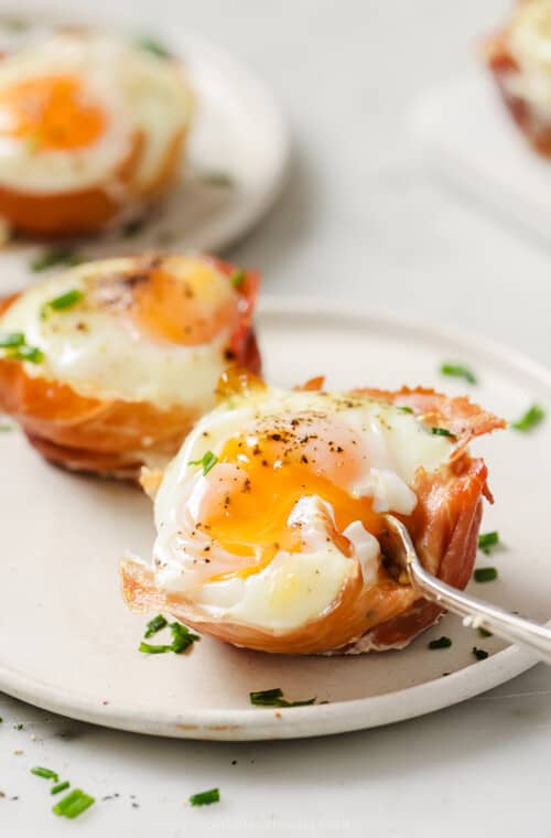 Digging into a prosciutto egg cup with a fork, revealing a runny yolk.