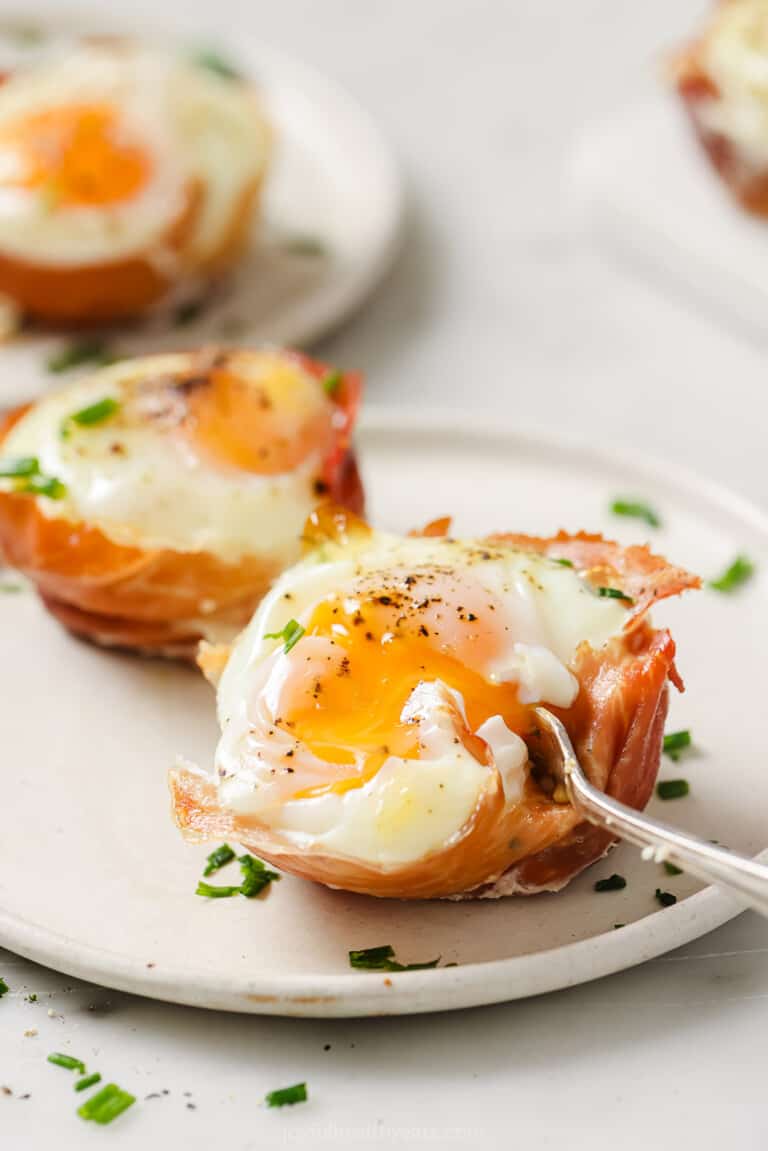 Digging into a prosciutto egg cup with a fork, revealing a runny yolk.