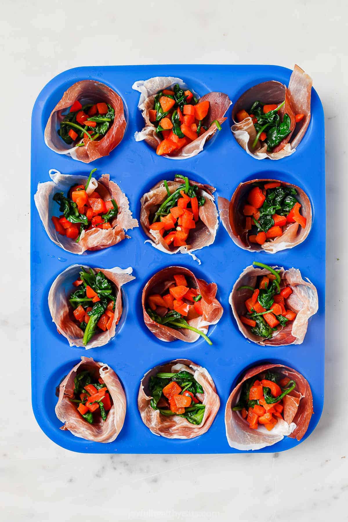 Prosciutto-lined muffin tray with spinach filling inside. 