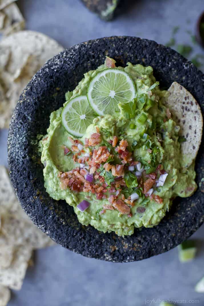 Guacamole in a bowl topped with bacon and lime slices