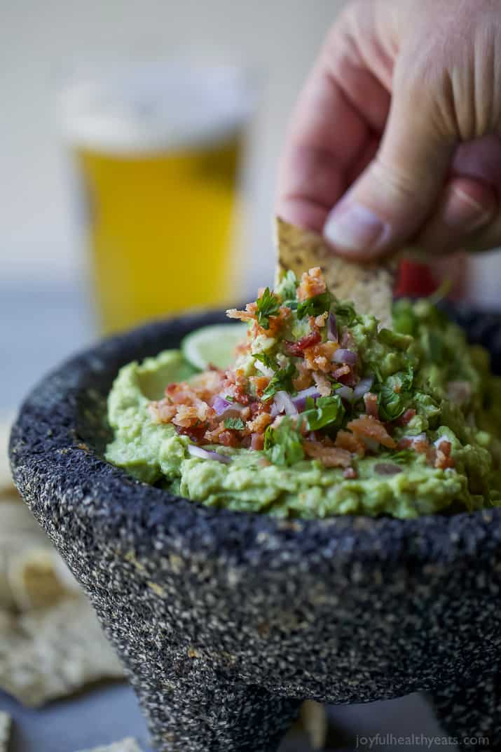 A chip being dipped into a bowl of Creamy Bacon Guacamole