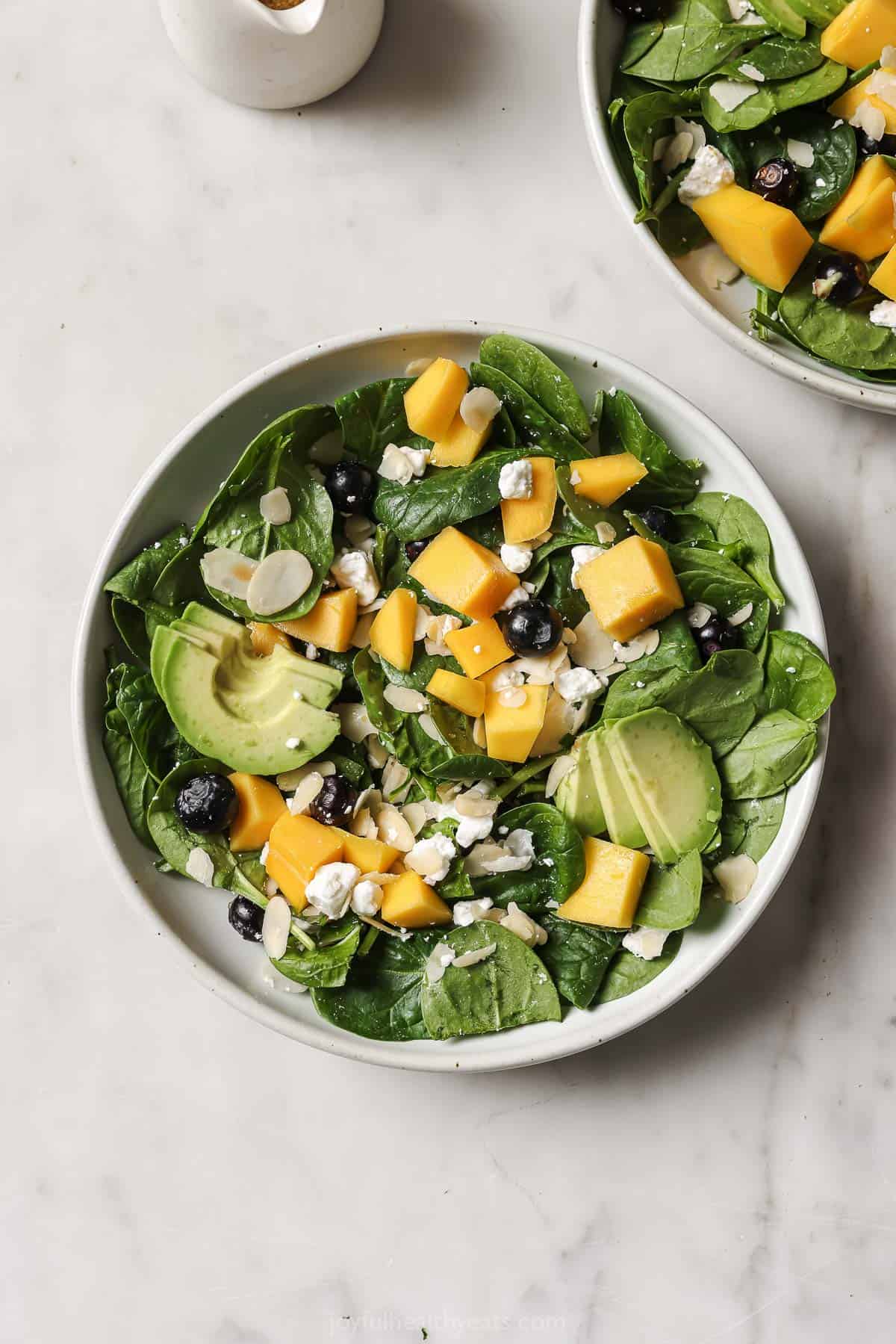 Bowl of baby spinach, avocado, mango, blueberries, goat cheese, and almonds. 