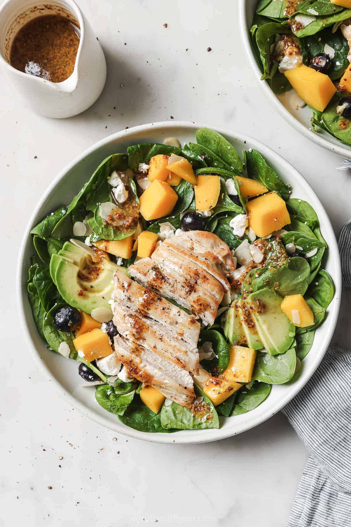 Bowl of salad with mango, chicken, blueberries, and baby spinach. 