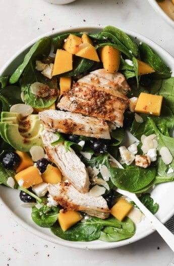 Bowl of avocado salad with mango, blueberries, grilled chicken, and goat cheese.