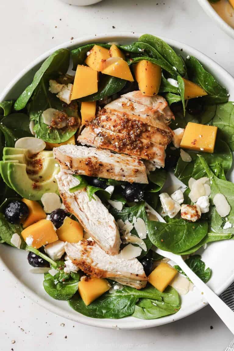 Bowl of avocado salad with mango, blueberries, grilled chicken, and goat cheese.