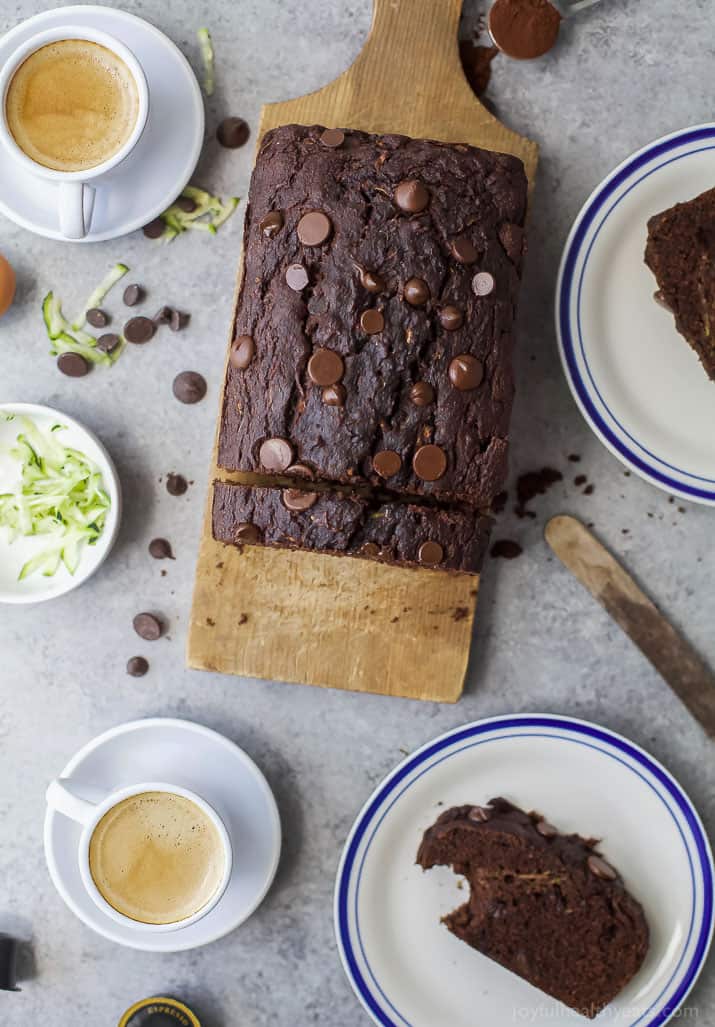 This tender chocolate zucchini bread recipe with maple syrup, applesauce, and dark chocolate chips will be your new favorite breakfast. Whole chocolate zucchini bread on a wooden chopping board.