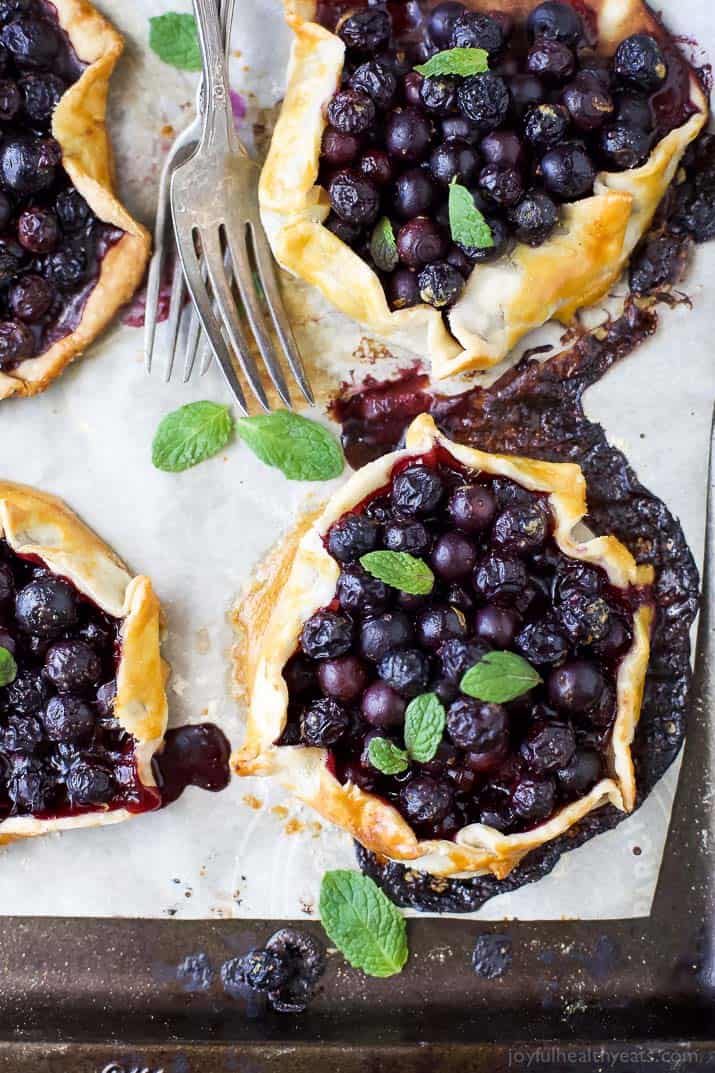 Top view of four Fresh Mini Blueberry Galettes on a parchment-lined baking sheet