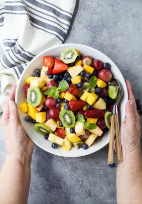 the best summer fruit salad in a bowl with hands holding the bowl