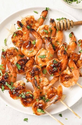 Plate of honey garlic shrimp skewers with cilantro on top.