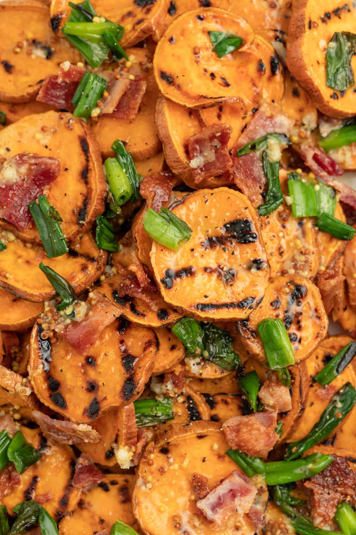 This 30-minute grilled sweet potato salad with bacon and honey mustard dressing is an easy side you'll be making on repeat this summer. Close-up of sweet potato salad with grill marks and sliced green onions.