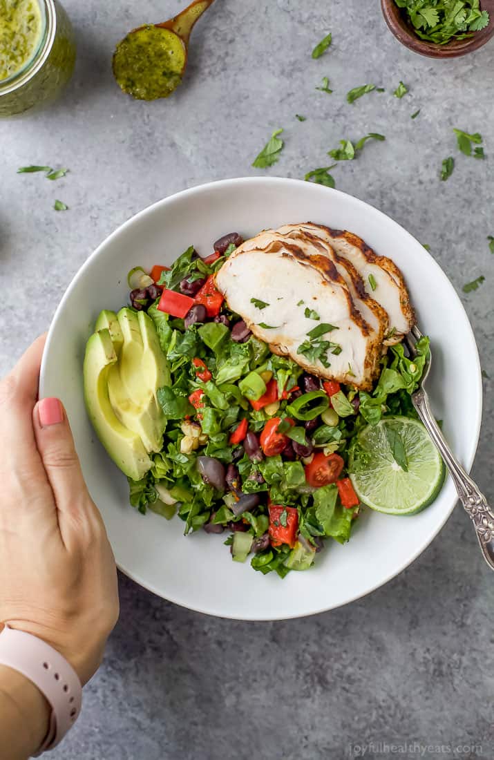 A hand on a white bowl filled with Mexican Chopped Salad with Grilled Chicken 