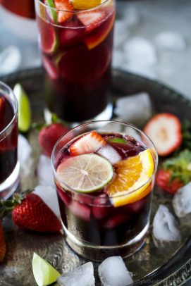 Three glasses of red wine sangria garnished with fresh fruit served on a metal tray.