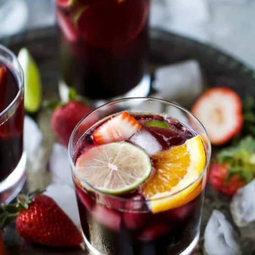 Three glasses of red wine sangria garnished with fresh fruit served on a metal tray.