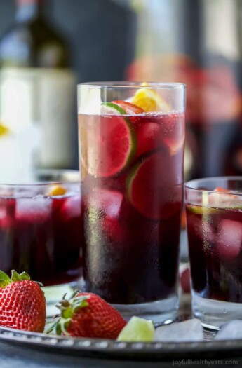 Three glasses of red wine sangria garnished with fresh fruit served on a metal tray.