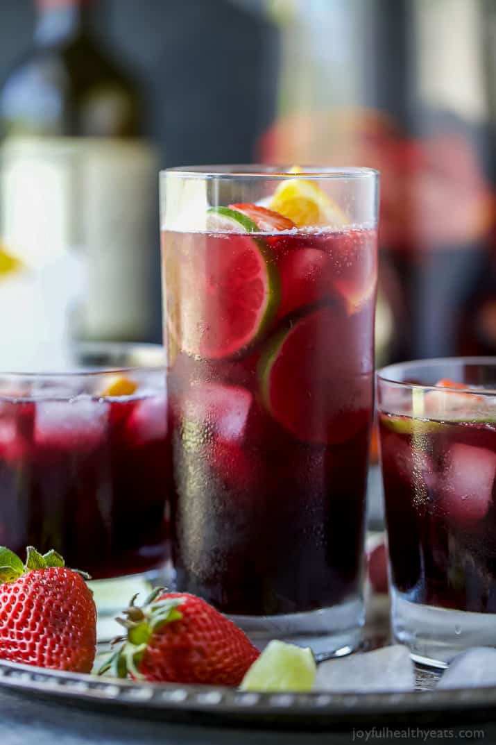 Three glasses of red wine sangria garnished with fresh fruit served on a metal tray.