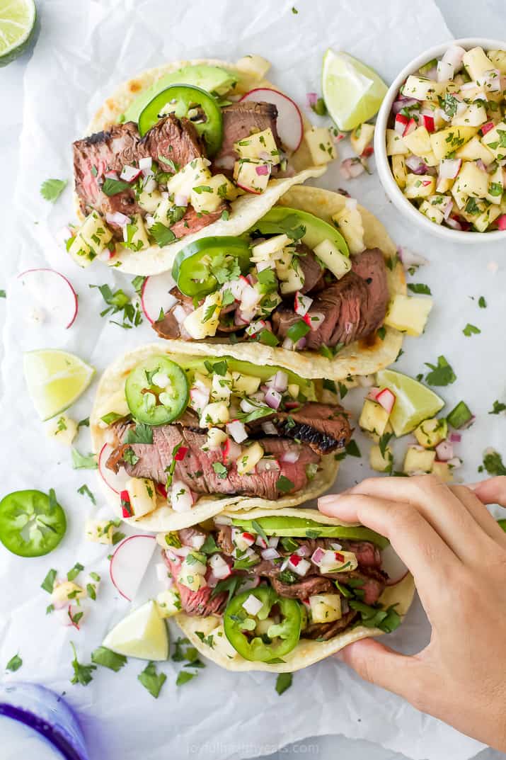 hand grabbing steak tacos with pineapple salsa