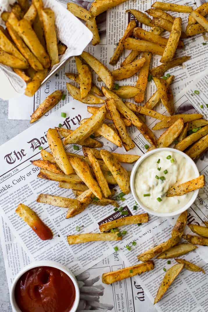 Top view of Crispy Oven Baked Fries on newspaper with a cup of Roasted Garlic Aioli