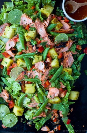 A salmon salad on a black serving platter with a small dish full of honey sriracha dressing