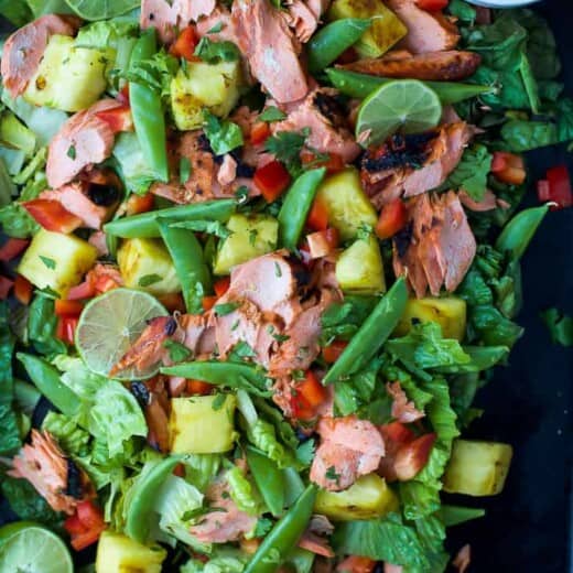 A salmon salad on a black serving platter with a small dish full of honey sriracha dressing