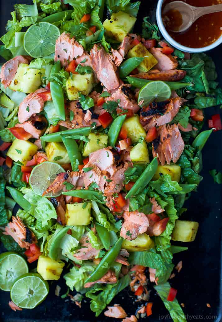 A salmon salad on a black serving platter with a small dish full of honey sriracha dressing.