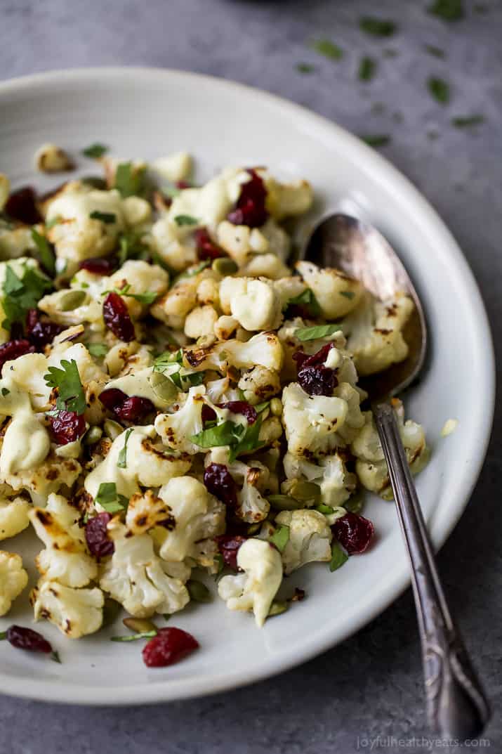 Roasted Cauliflower Salad tossed with a Curry Yogurt Sauce, dry cranberries and pepitas! This healthy salad is easy to make and loaded with flavor! It's the perfect side dish to bring to your next party - definitely a conversation starter.