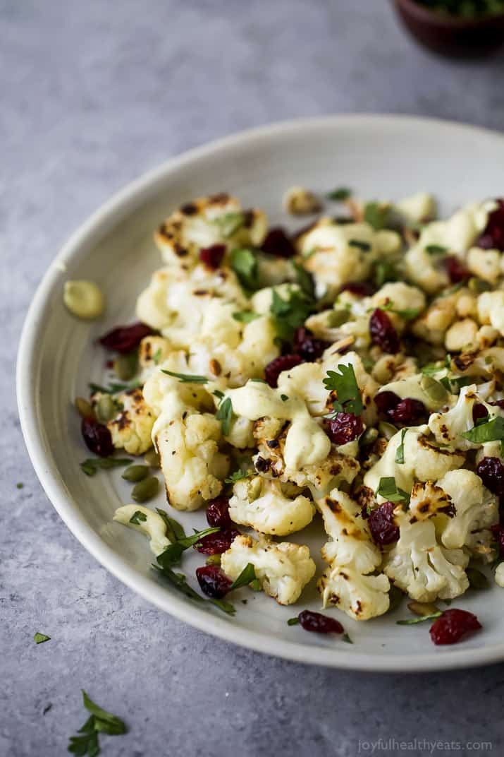 Roasted Cauliflower Salad tossed with a Curry Yogurt Sauce, dry cranberries and pepitas! This healthy salad is easy to make and loaded with flavor! It's the perfect side dish to bring to your next party - definitely a conversation starter.