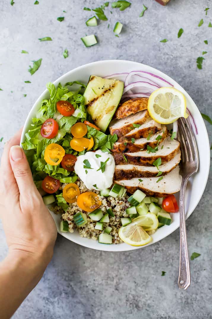 A hand grabbing a chicken shawarma bowl from a granite countertop