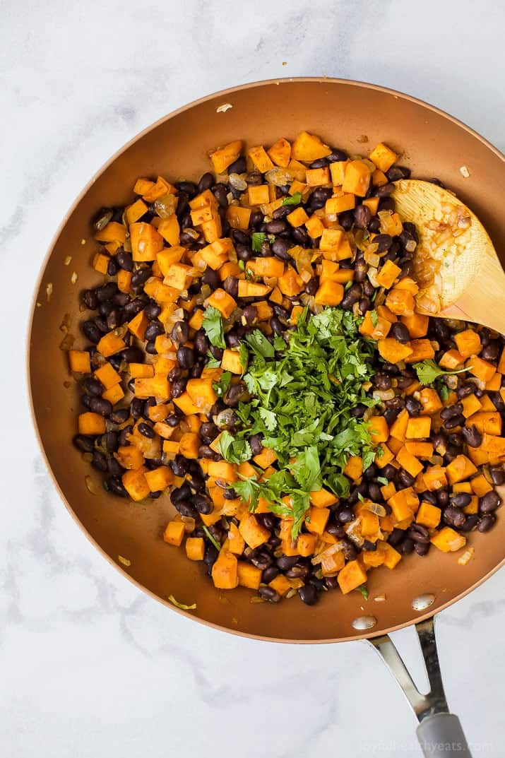 This saucy sweet potato black bean enchiladas recipe with smokey seasonings, spicy salsa, and melty cheese is an easy Tex-Mex dinner. Sautéed filling in the pan.