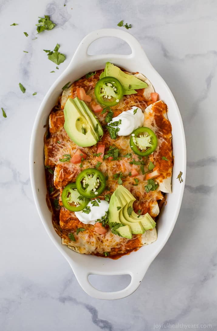 Cheesy Tex-Mex enchiladas with sour cream, jalapeños, cilantro, and avocado on top.