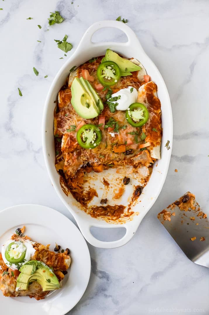 Sweet ،ato black bean enchiladas topped with cilantro, sliced avocado, and jalapeños in the baking dish. 