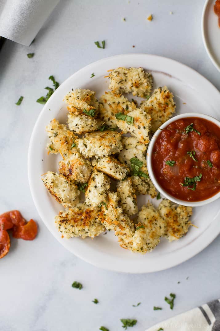 Top view of Baked Chicken Parmesan Bites with a cup of homemade marinara sauce on a plate