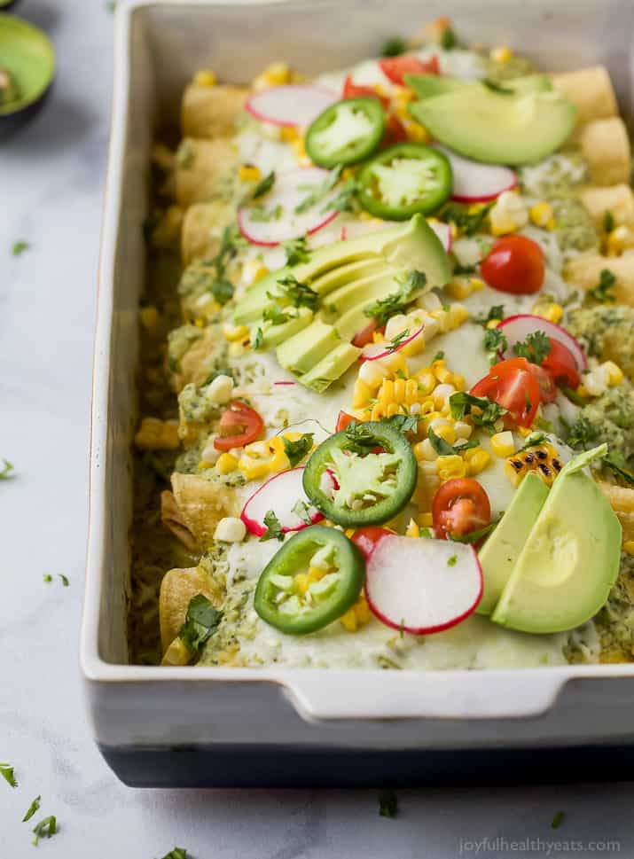 Chicken Enchiladas in a baking dish topped with Poblano Cream Sauce and fresh avocado, tomato, corn, jalapeno, and radishes