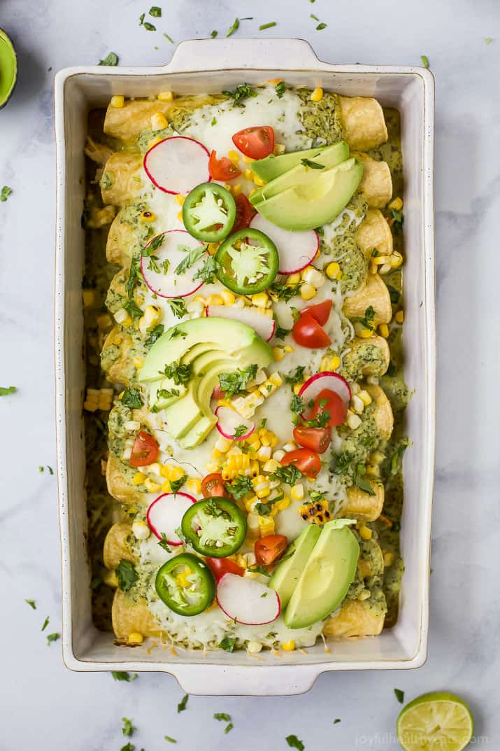 Chicken Enchiladas in a baking dish topped with Poblano Cream Sauce, fresh avocado, corn, tomato, and radishes