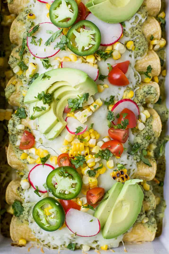 Close-up of Chicken Enchiladas topped with Poblano Cream Sauce and fresh avocado, corn, tomatoes, jalapenos and radishes