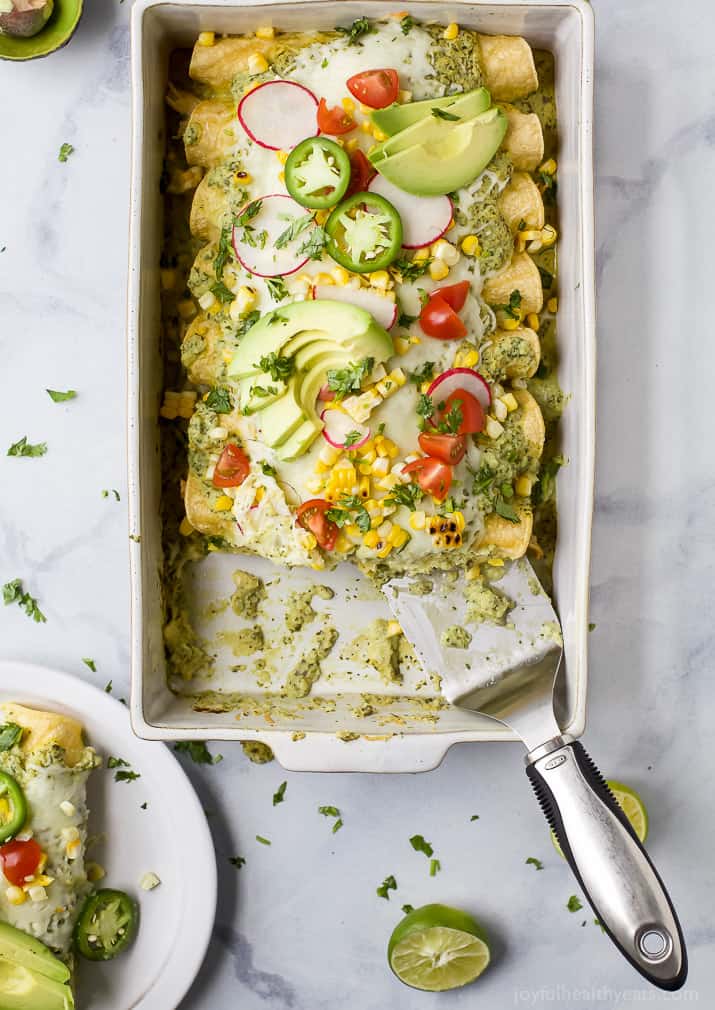 Top view of Chicken Enchiladas in a baking dish topped with Poblano Cream Sauce and fresh veggies