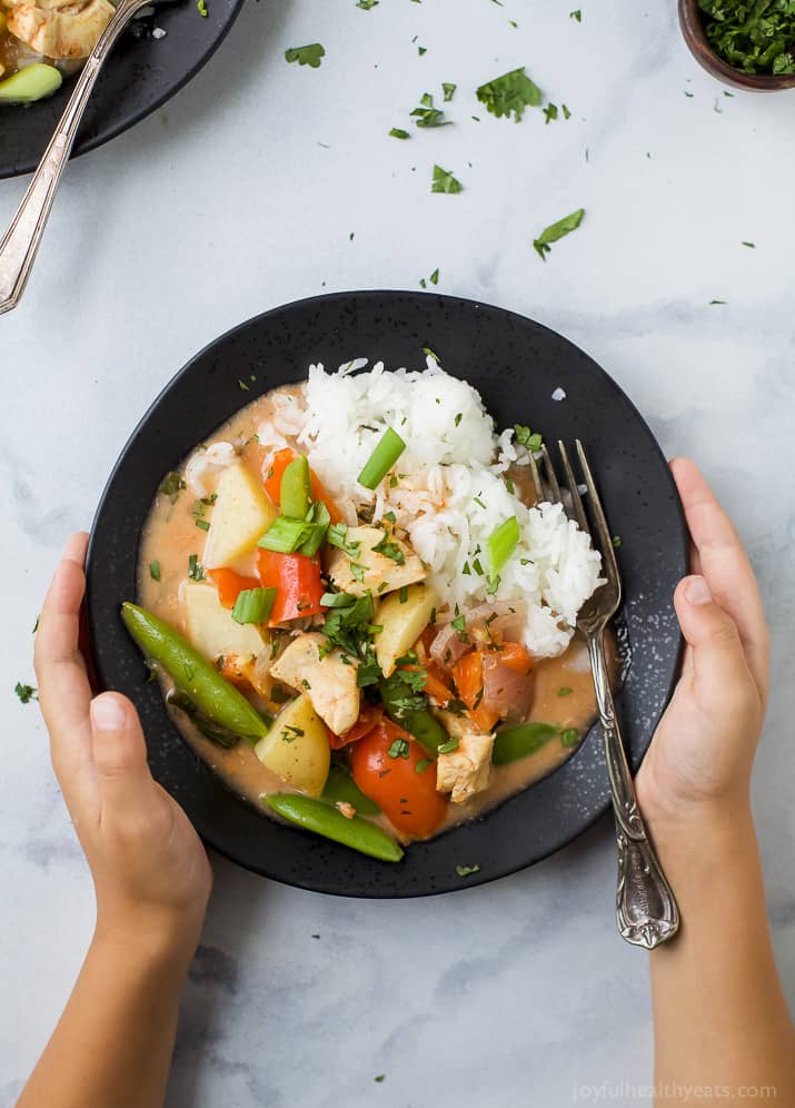 Top view of hands holding a bowl of Chicken Curry with white rice