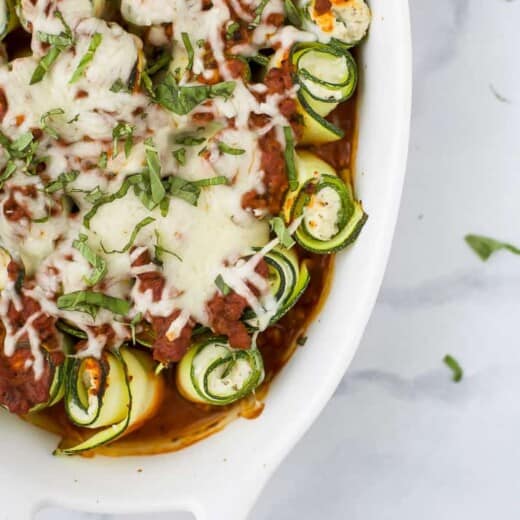 Angled photo of baked zucchini rolls with ricotta and tomato sauce.