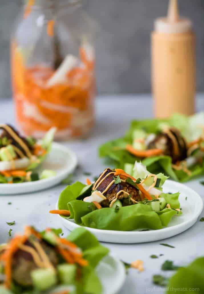 Banh Mi Lettuce Wraps on plates with turkey meatballs, pickled vegetables and sriracha mayo on a lettuce wrap