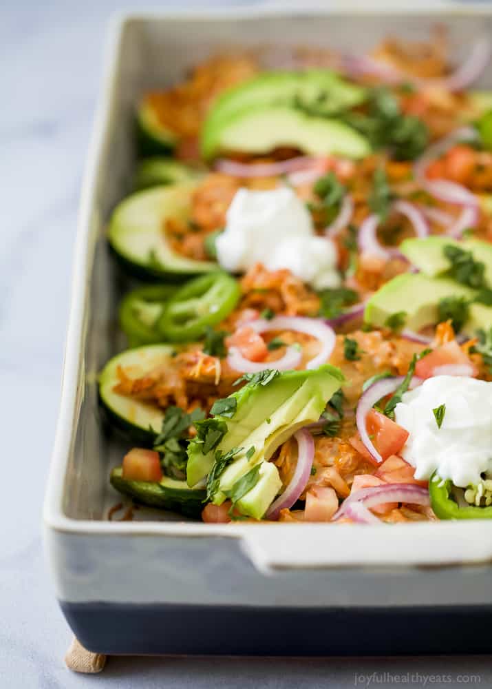 Close-up view of a pan of Chicken Enchilada Zucchini Boats topped with avocado, red onion, sour cream and fresh herbs