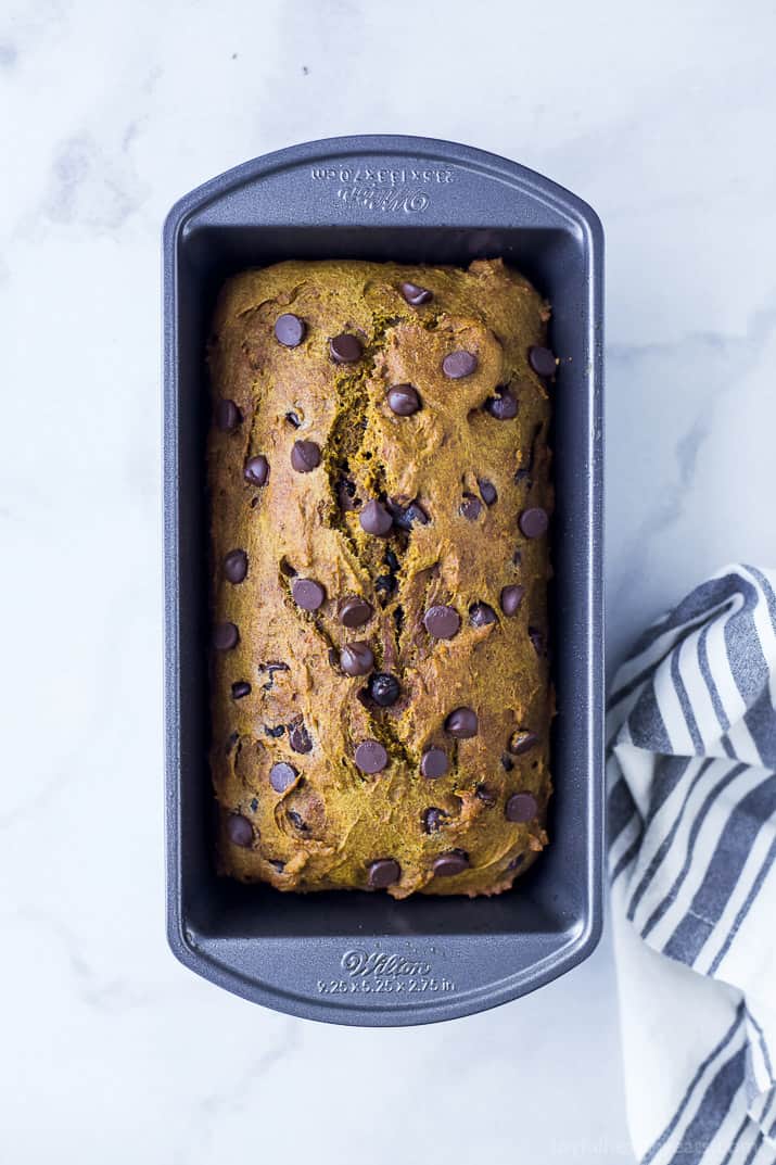 A loaf of chocolate chip pumpkin bread in a pan on top of a marble counter
